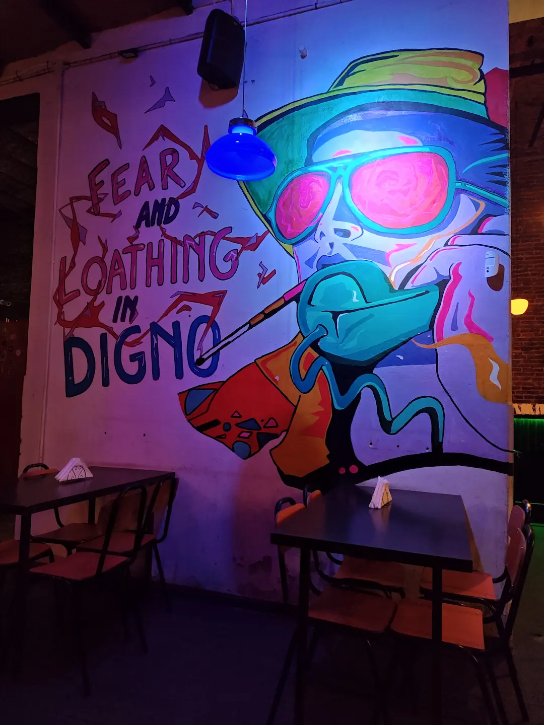 Mural artístico urbano y mesas en el sector interior de Digno Bar