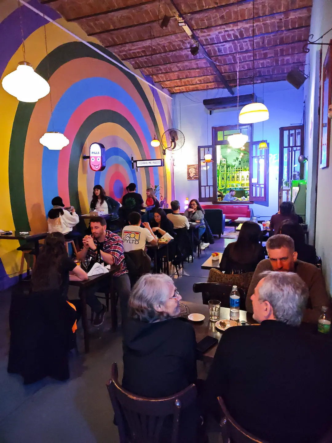 Mesas y salón interior con mural de arcos retro en Digno Bar Zeballos