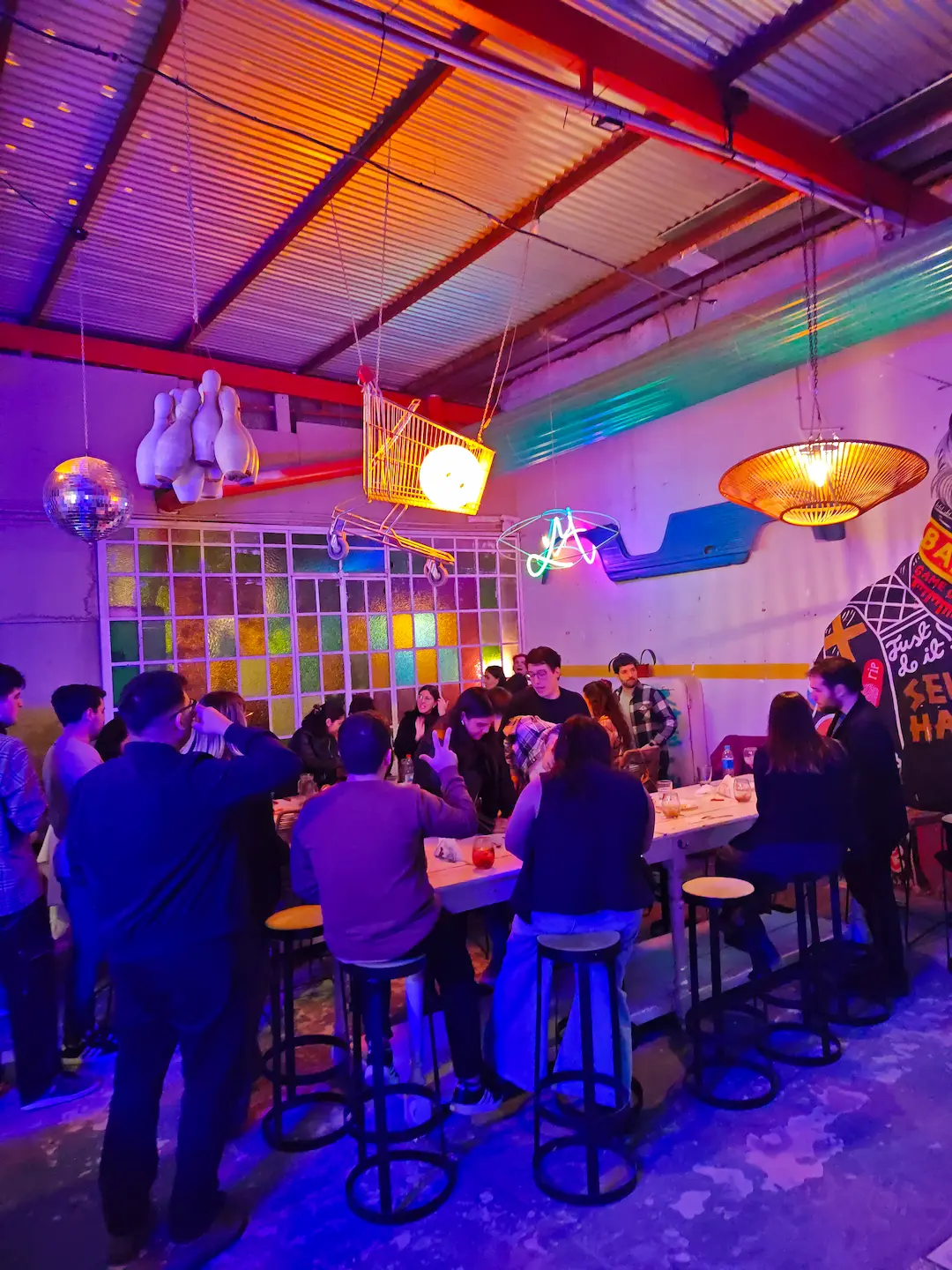 Espacio amplio con mesas comunitarias altas y barra iluminada en Zeballos
